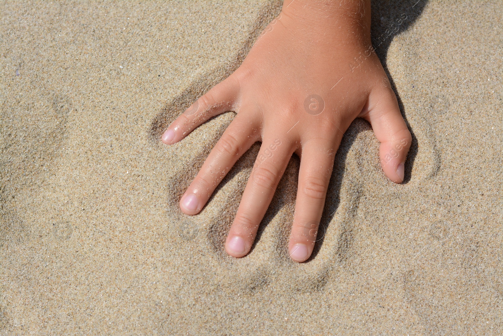 Photo of Child leaving handprint on sand outdoors, closeup. Fleeting time concept