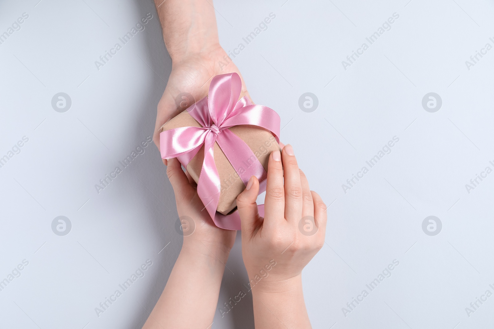 Photo of Man giving gift box to woman on light gray background, top view