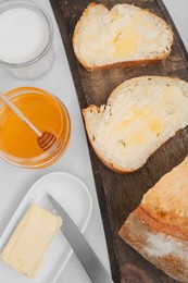 Photo of Sandwiches with butter, honey and milk on white table, flat lay