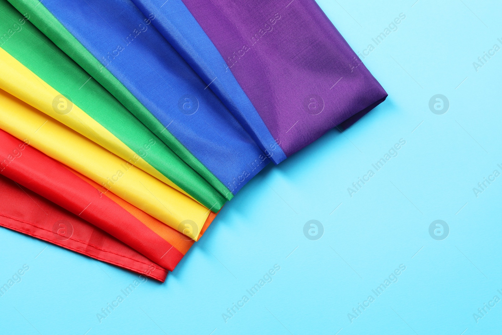 Photo of Rainbow LGBT flag on light blue background, top view. Space for text