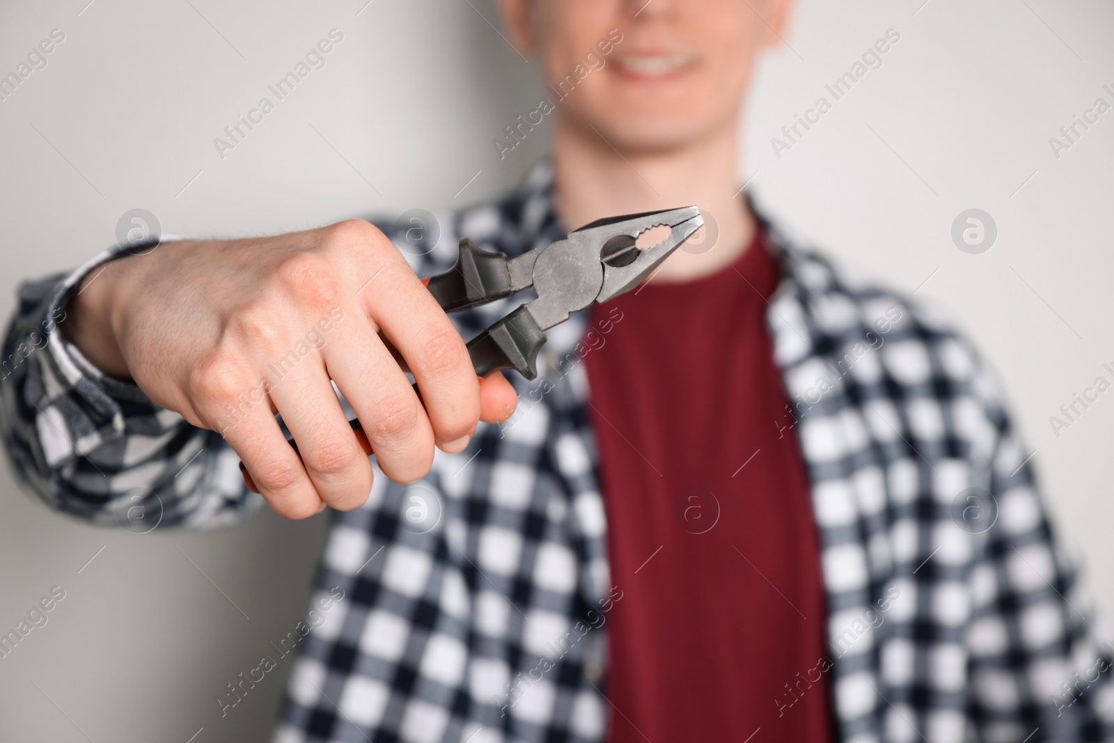 Photo of Handyman with pliers against light background, focus on hand