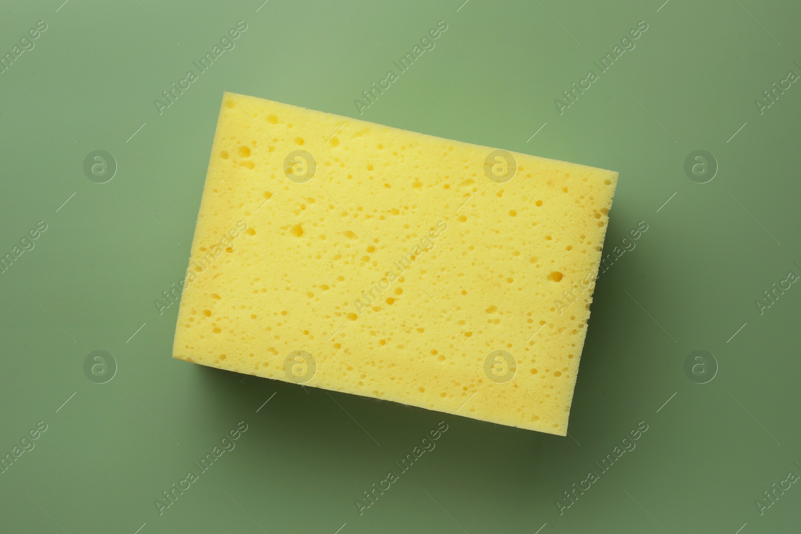 Photo of New yellow sponge on green background, top view