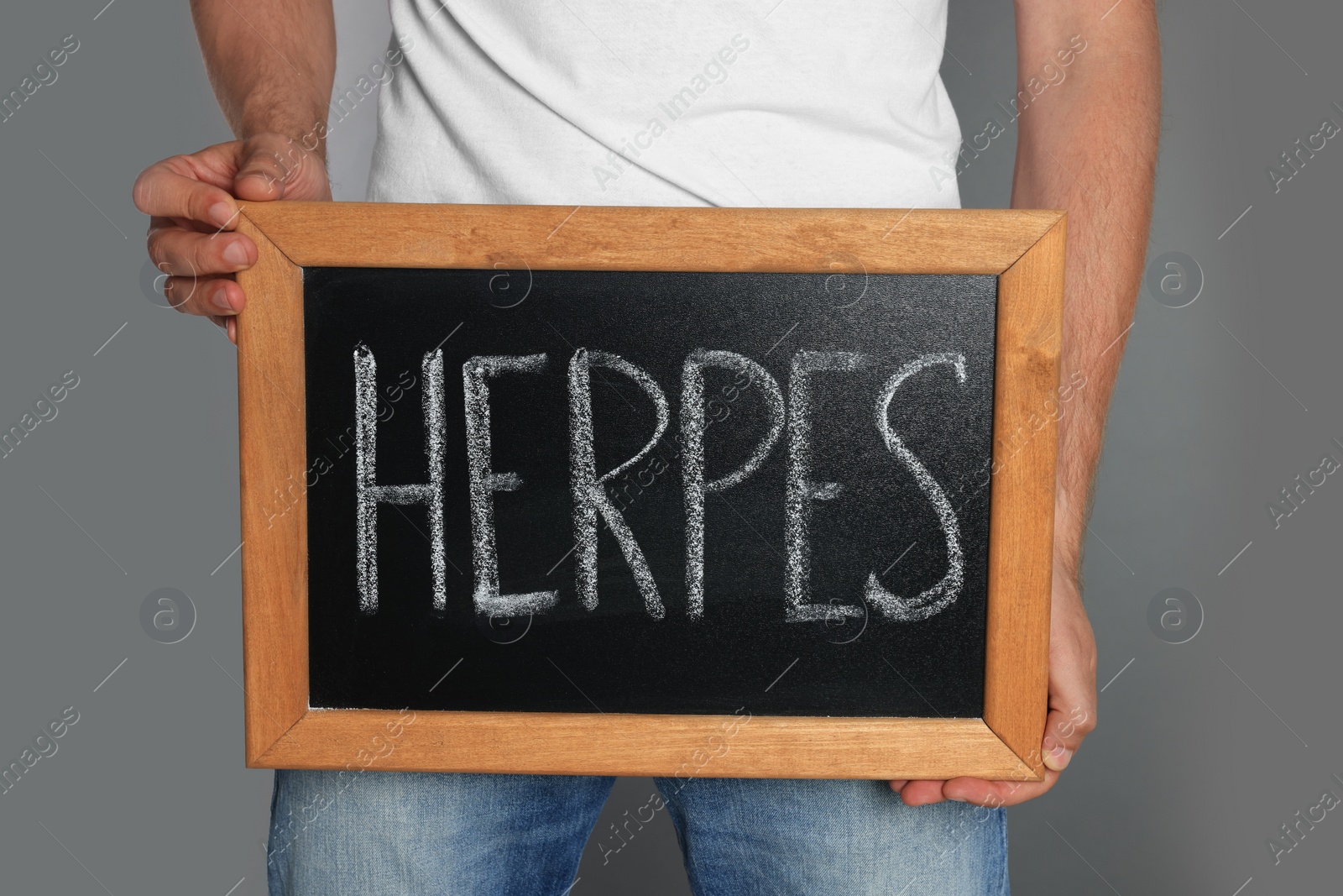 Photo of Man holding small chalkboard with word Herpes on grey background