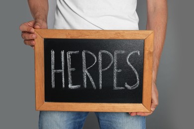 Man holding small chalkboard with word Herpes on grey background