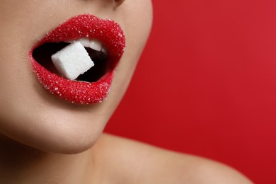 Woman with beautiful lips eating sugar cube on red background, closeup. Space for text
