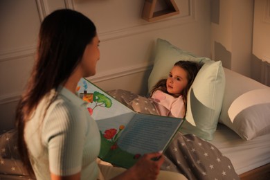 Photo of Mother reading bedtime story to her daughter at home