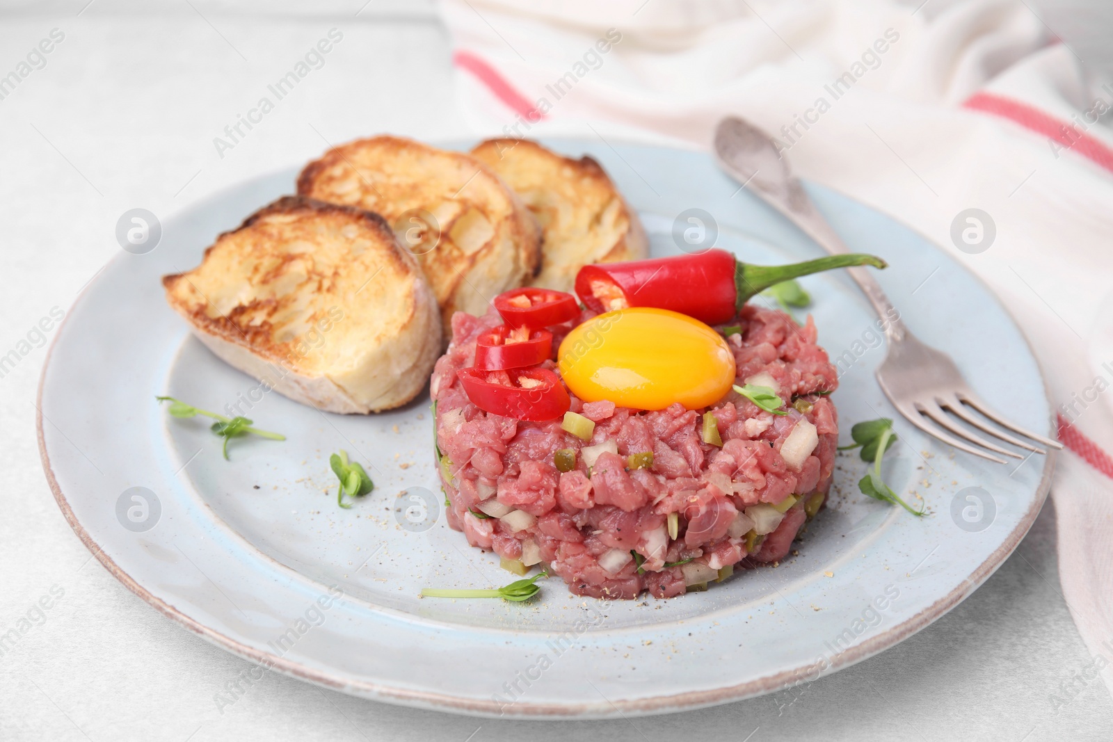 Photo of Tasty beef steak tartare served with yolk and other accompaniments on white table