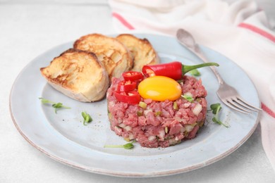 Tasty beef steak tartare served with yolk and other accompaniments on white table