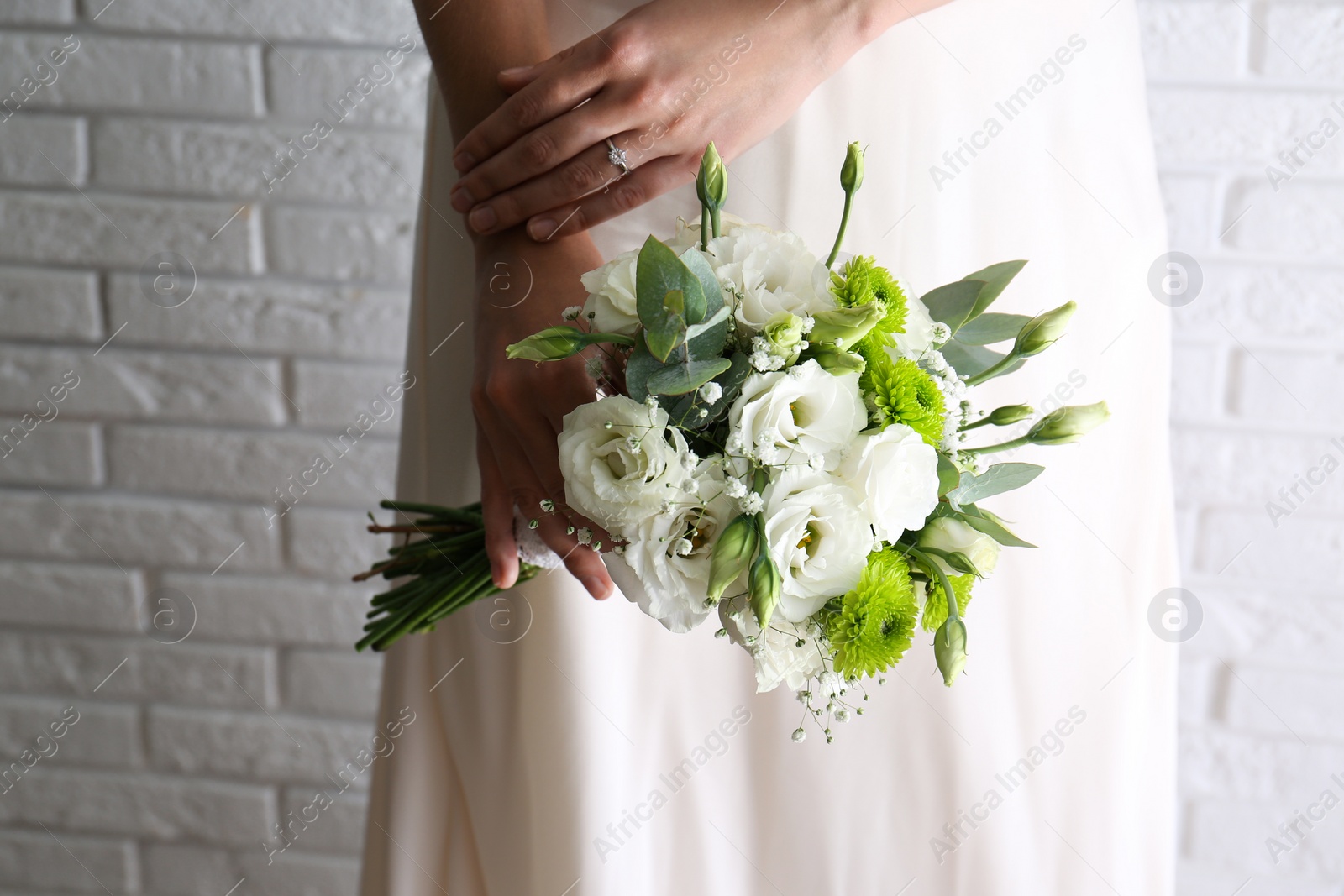 Photo of Bride holding beautiful bouquet with Eustoma flowers near brick wall, closeup