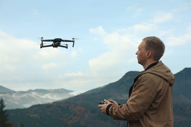 Young man operating modern drone with remote control in mountains