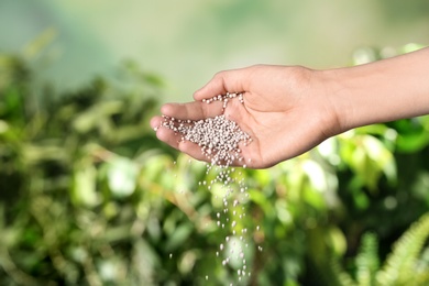 Photo of Woman pouring fertilizer on blurred background, closeup with space for text. Gardening time