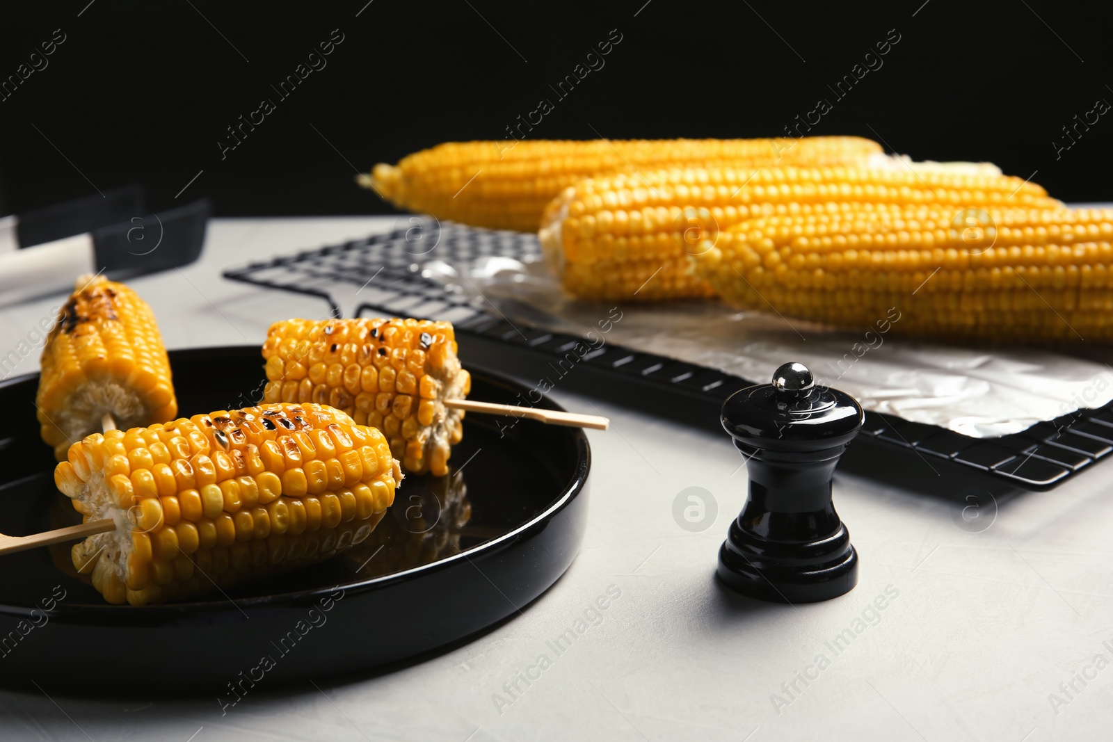 Photo of Ceramic plate with grilled corn cobs on light table