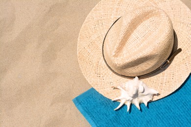 Soft blue beach towel with straw hat and seashell on sand, flat lay. Space for text