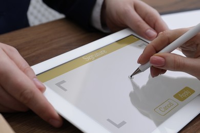 Electronic signature. Woman using stylus and tablet at wooden table, closeup