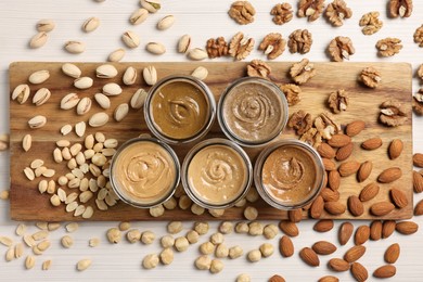 Many tasty nut butters in jars and nuts on white table, flat lay