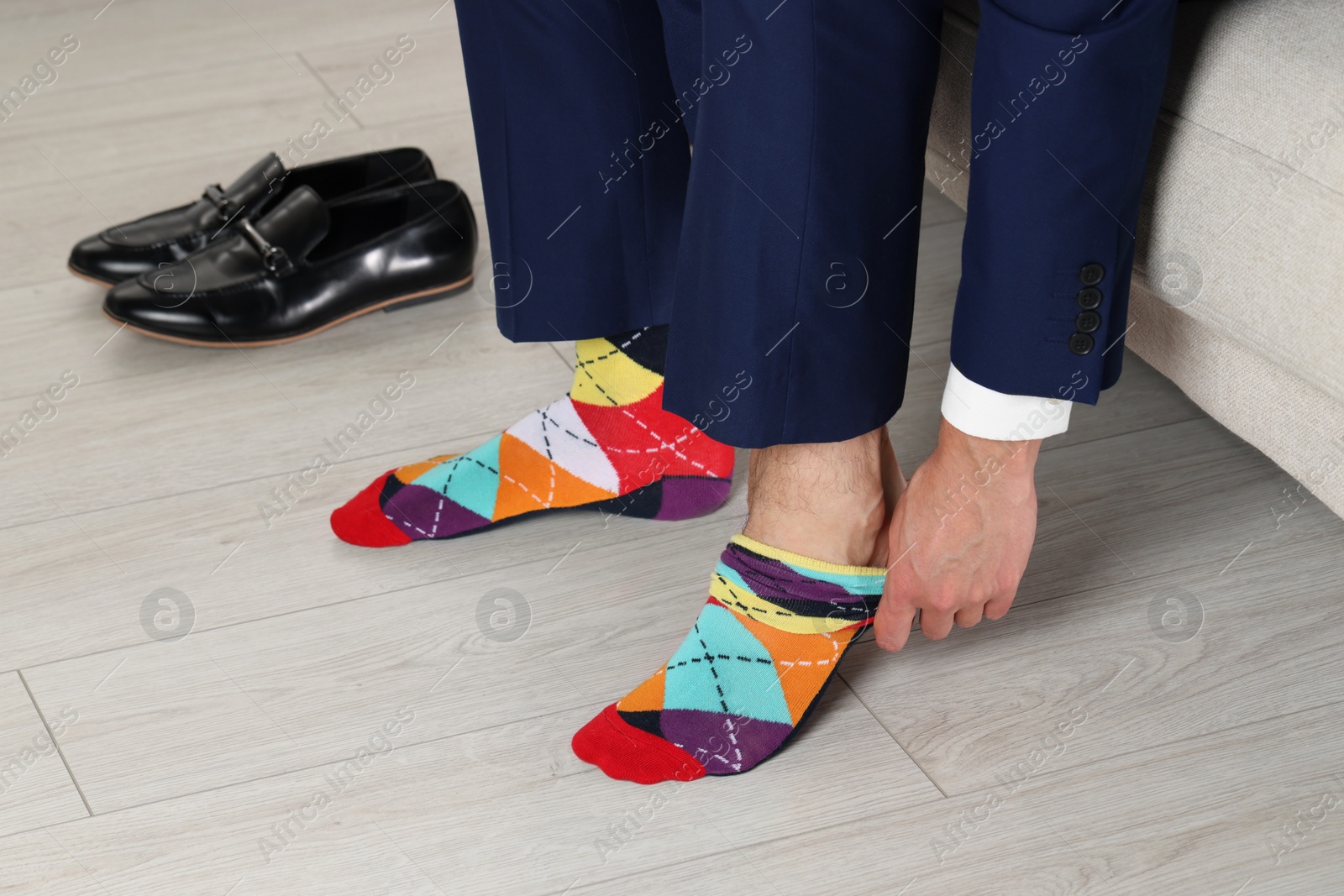 Photo of Man putting on colorful socks indoors, closeup