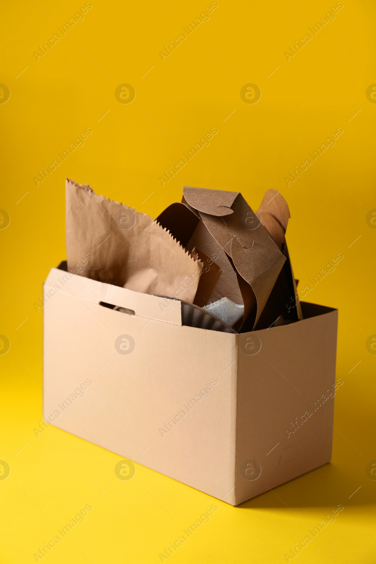 Photo of Box with waste paper on yellow background