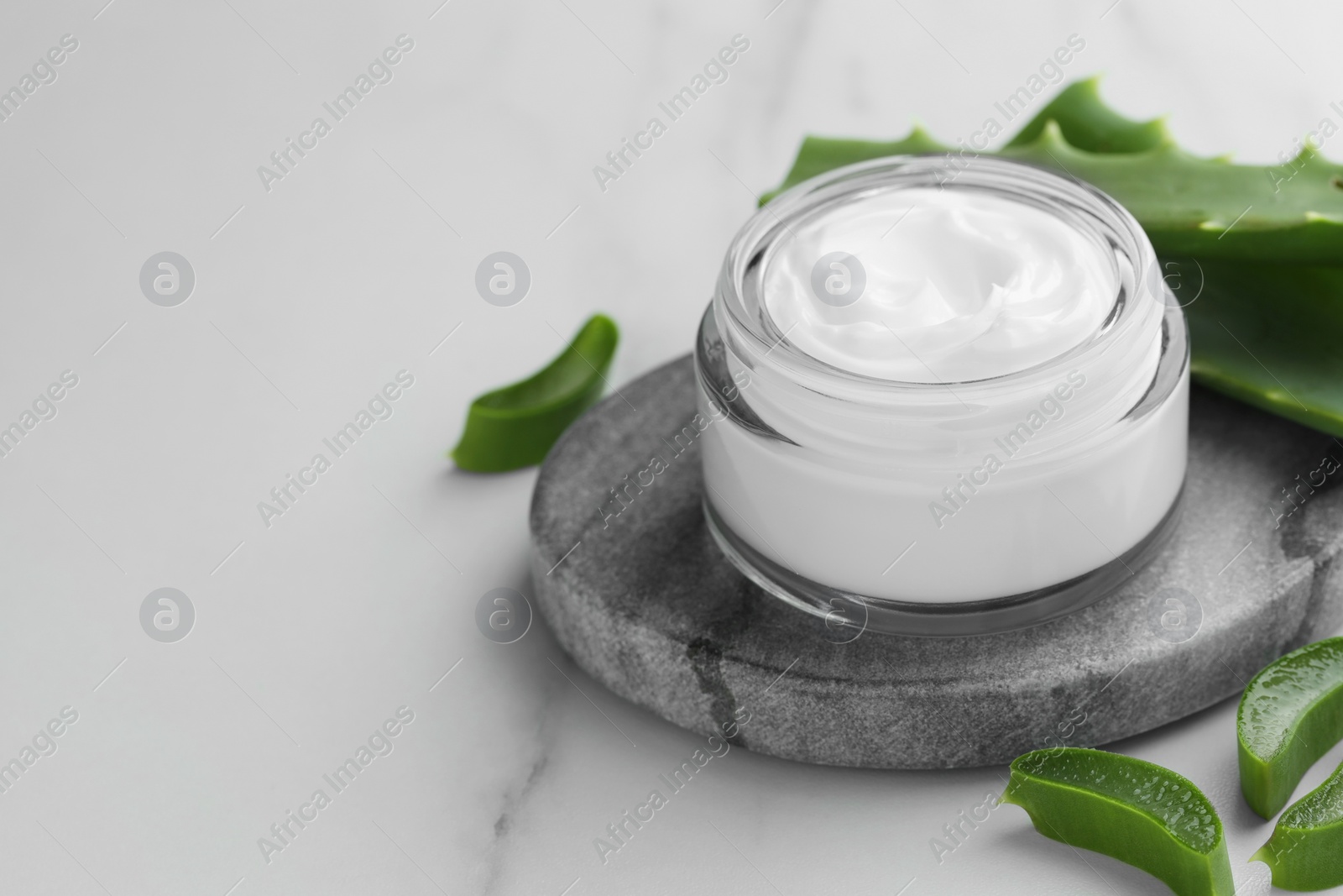 Photo of Jar with cream and cut aloe leaves on white marble table, closeup. Space for text