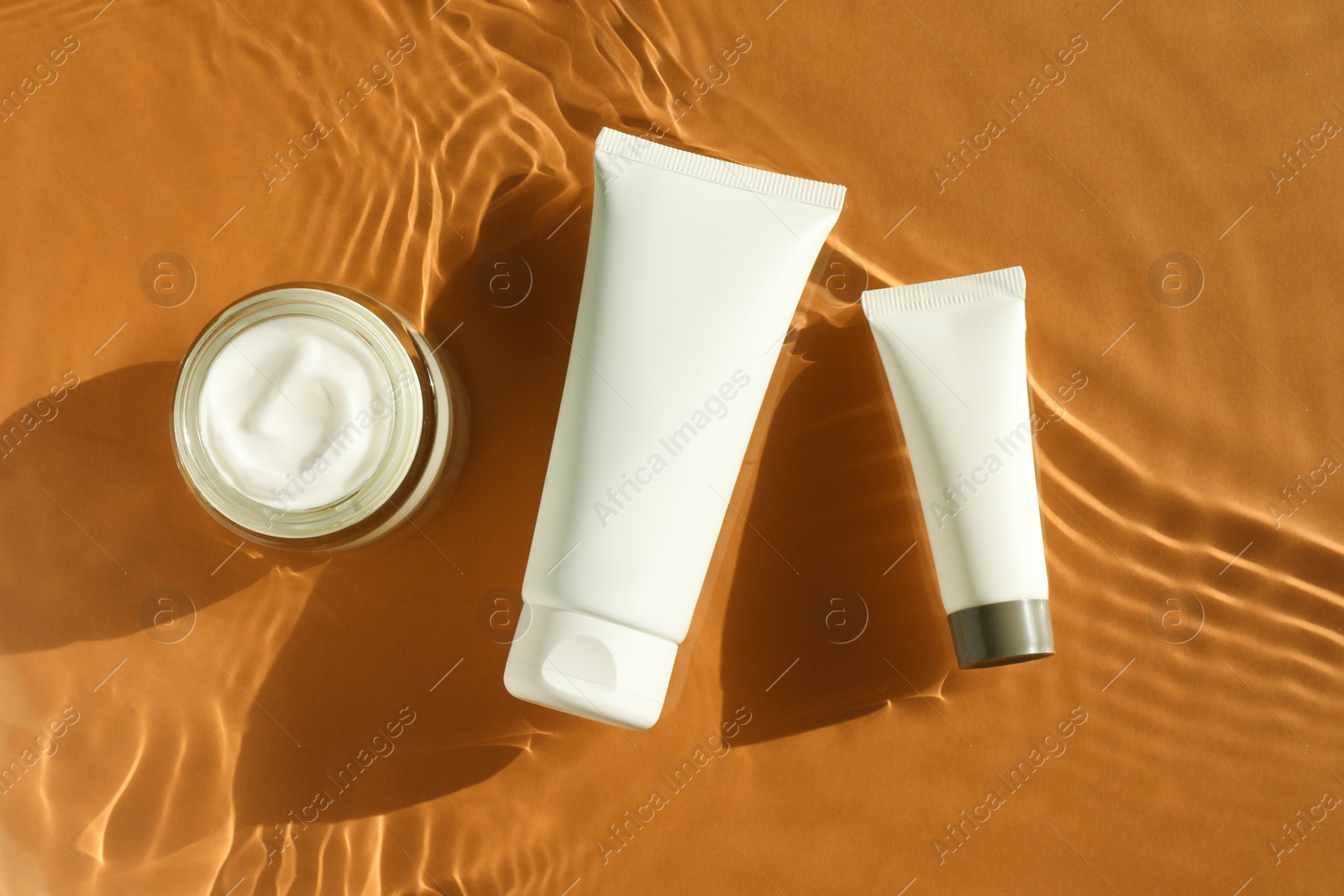 Photo of Tubes and jar with moisturizing cream in water on orange background, top view