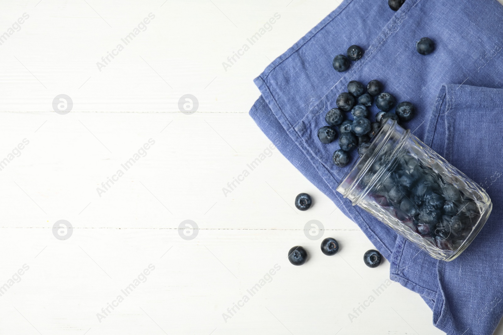 Photo of Overturned glass jar of ripe blueberries on white wooden table, flat lay. Space for text