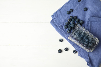 Photo of Overturned glass jar of ripe blueberries on white wooden table, flat lay. Space for text