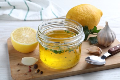 Photo of Jar with lemon sauce and ingredients on white wooden table. Delicious salad dressing