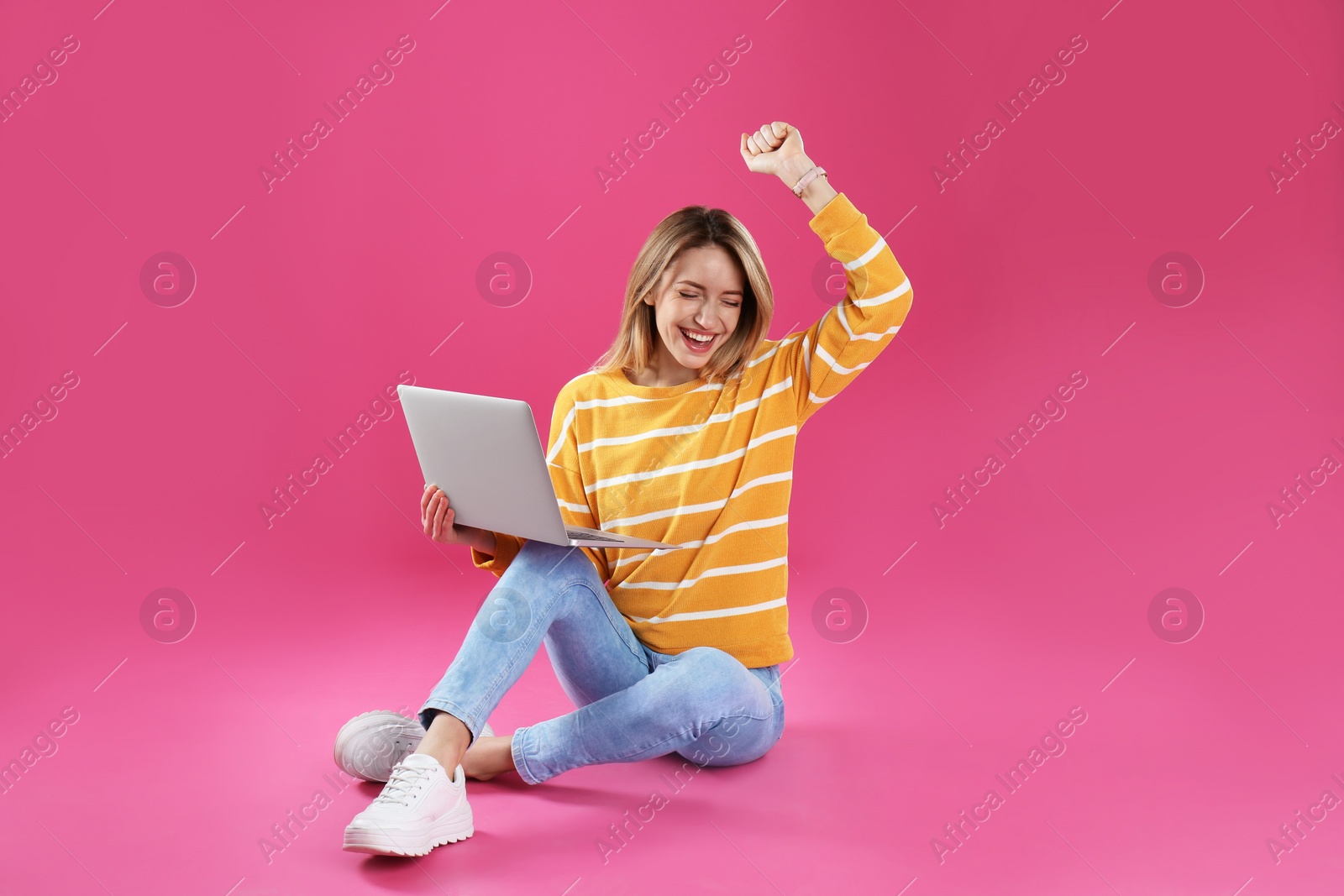 Photo of Happy young woman in casual outfit with laptop sitting on color background