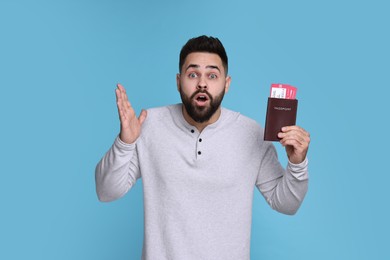 Surprised man with passport and tickets on light blue background