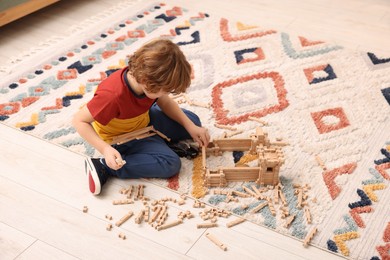 Little boy playing with wooden construction set on carpet in room. Child's toy