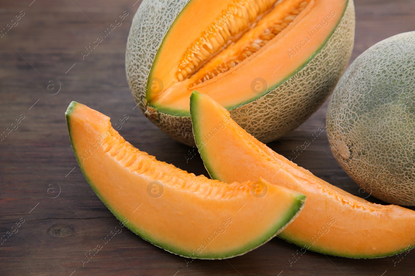 Photo of Whole and cut delicious ripe melons on wooden table, closeup