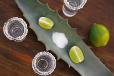 Photo of Mexican tequila shots, salt, lime and green leaf on wooden table, flat lay. Drink made of agava