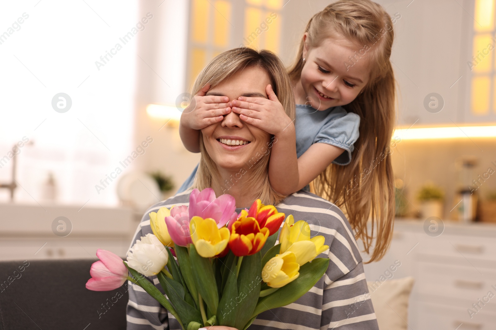 Photo of Little girl surprising her mom with bouquet of tulips at home. Happy Mother`s Day