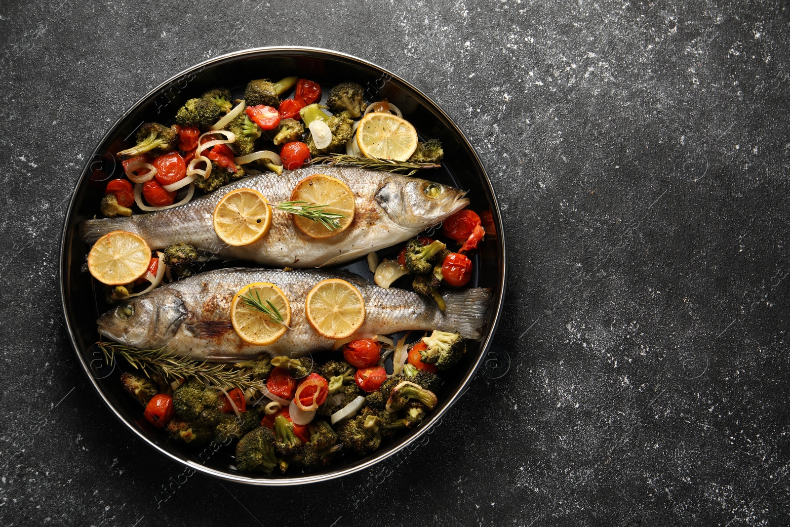 Photo of Baked fish with vegetables, rosemary and lemon on black textured table, top view. Space for text