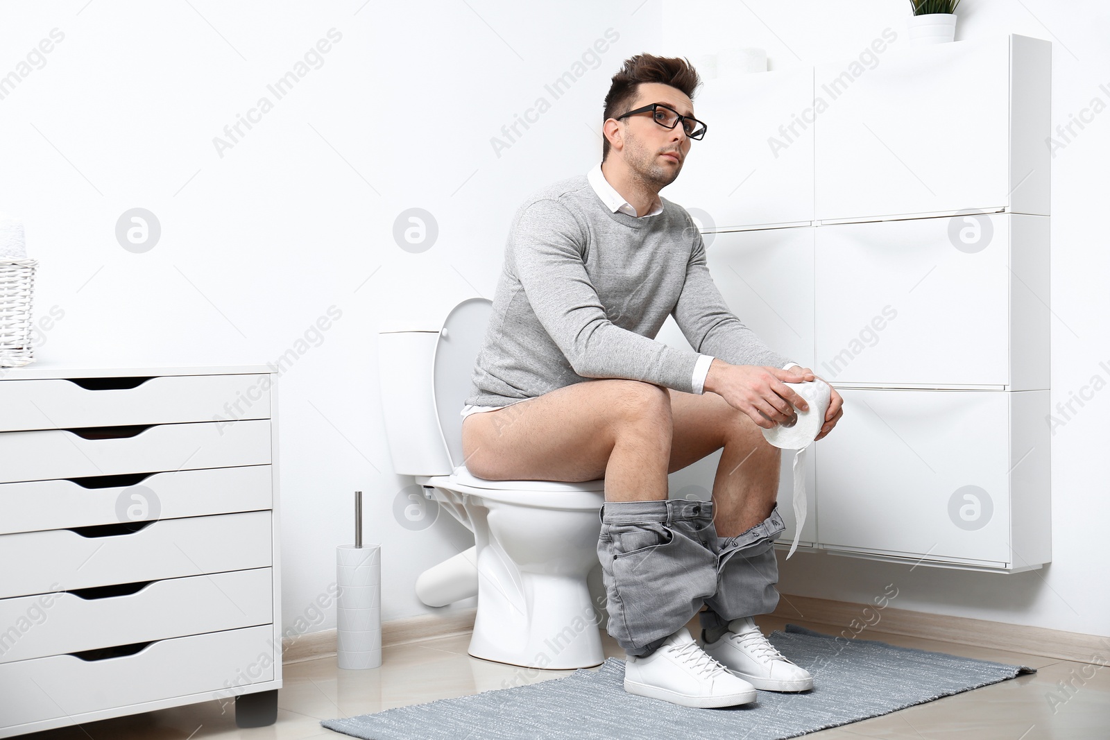 Photo of Man with paper roll sitting on toilet bowl in bathroom