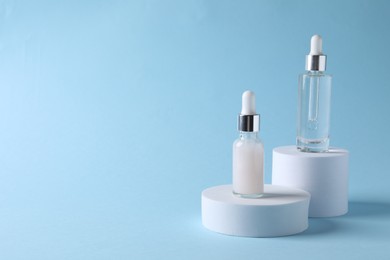 Presentation of bottles with cosmetic serums on light blue background, space for text