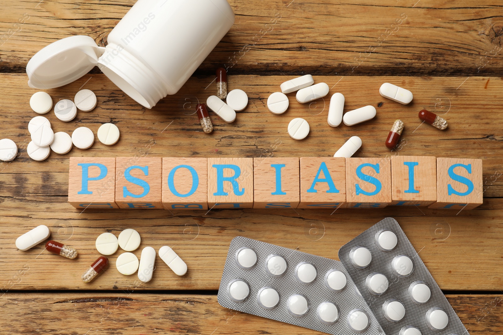 Photo of Word Psoriasis made of cubes with letters and pills on wooden table, flat lay