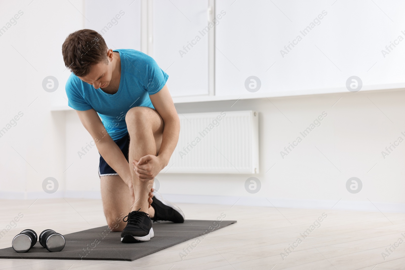 Photo of Man suffering from leg pain on mat indoors. Space for text