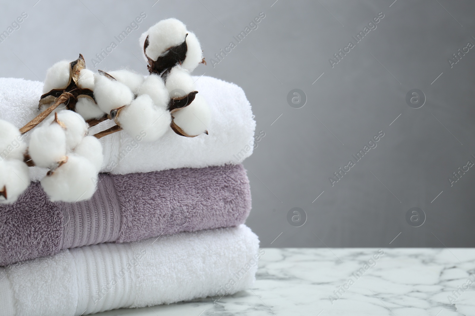 Photo of Stack of folded terry towels and cotton flowers on white marble table, closeup. Space for text