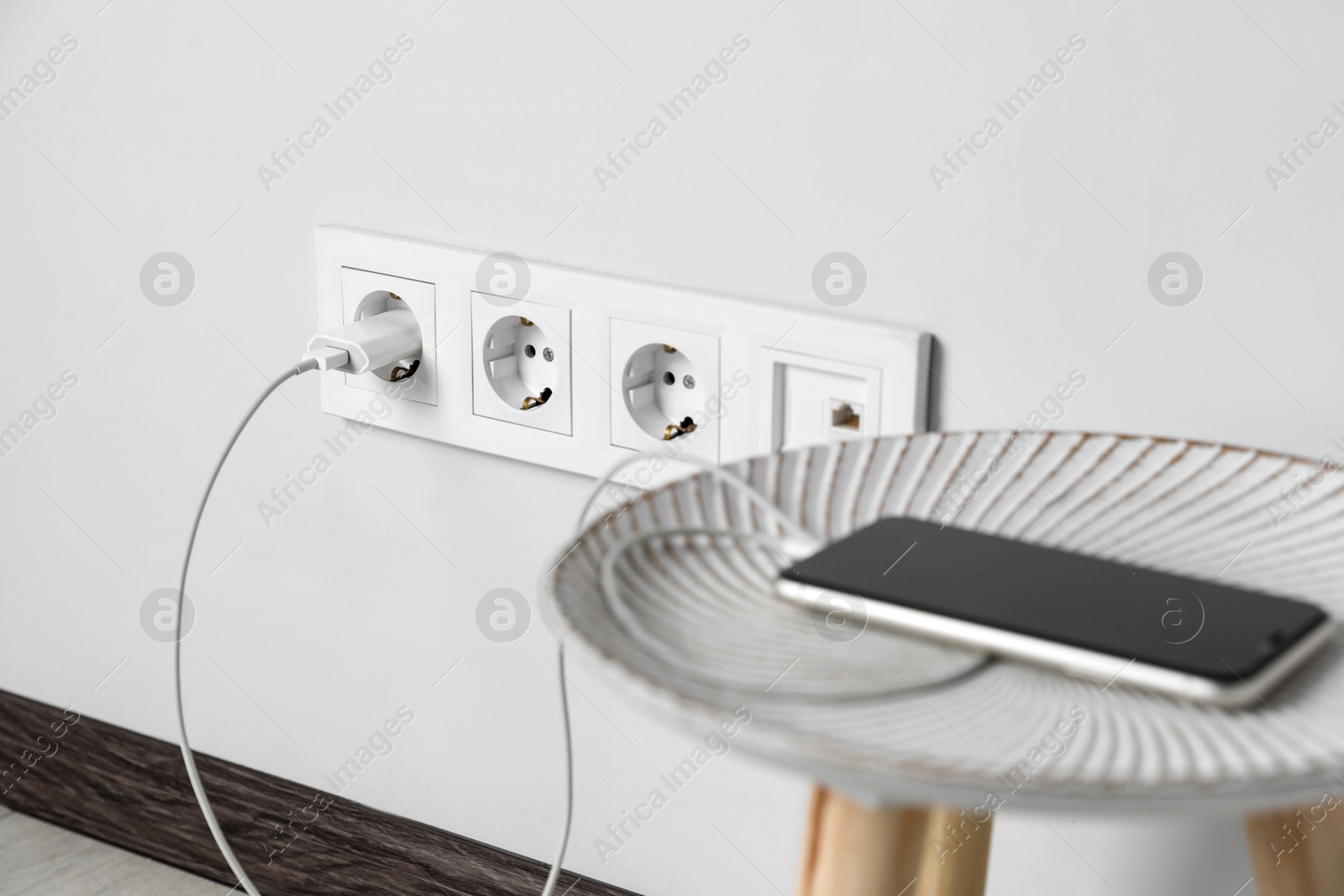 Photo of Modern smartphone charging from electric socket indoors, closeup