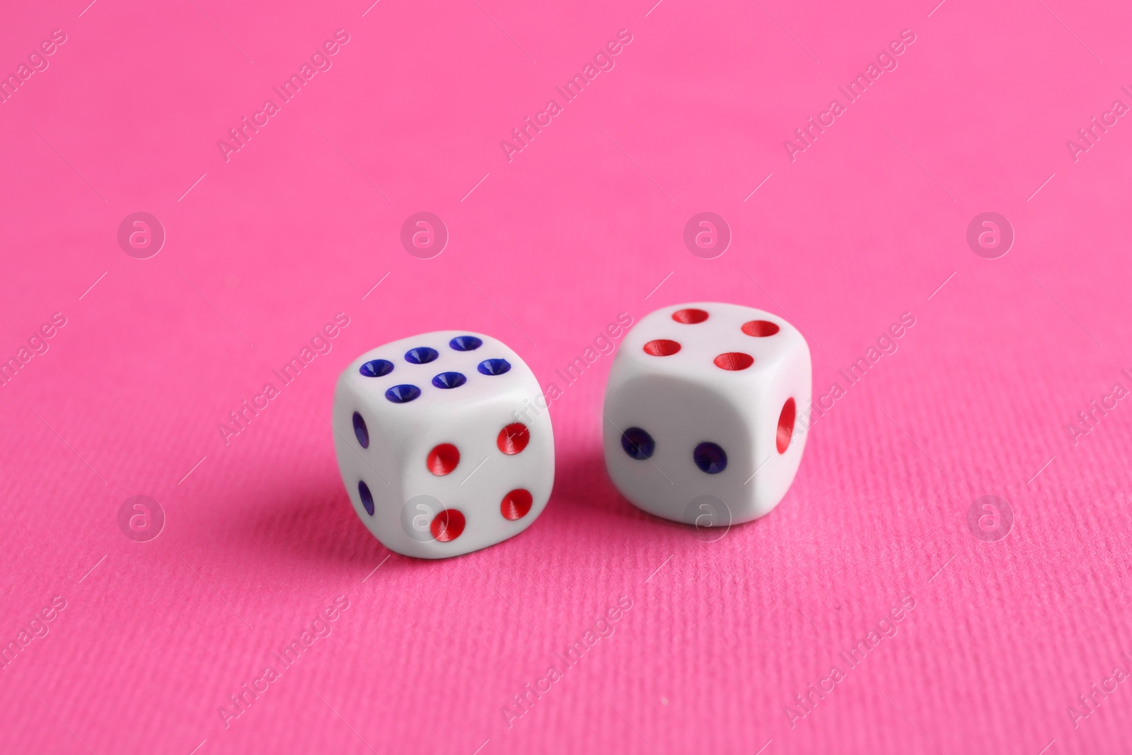 Photo of Two white game dices on pink background, closeup