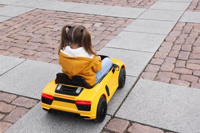 Cute little girl driving children's car on city street, back view. Space for text