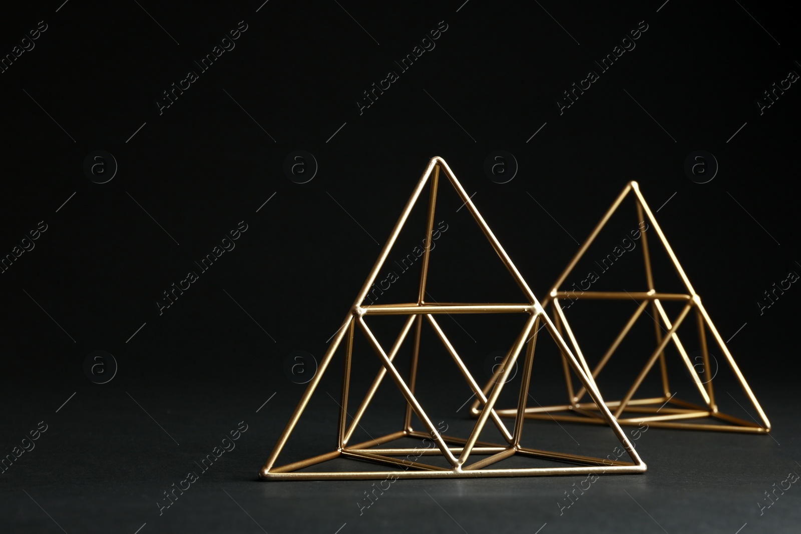 Photo of Shiny decorative gold pyramids on black background. Space for text