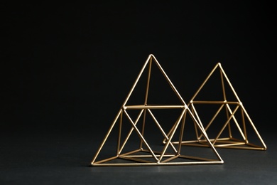 Photo of Shiny decorative gold pyramids on black background. Space for text