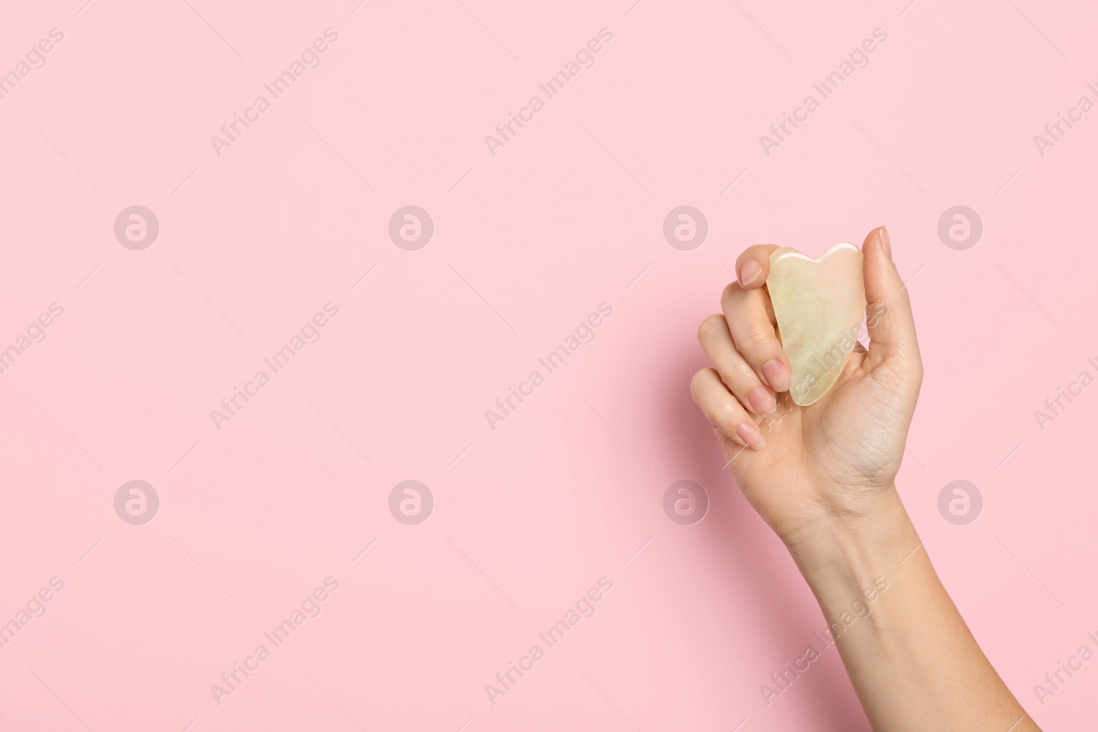 Photo of Woman with jade gua sha tool on light pink background, closeup. Space for text