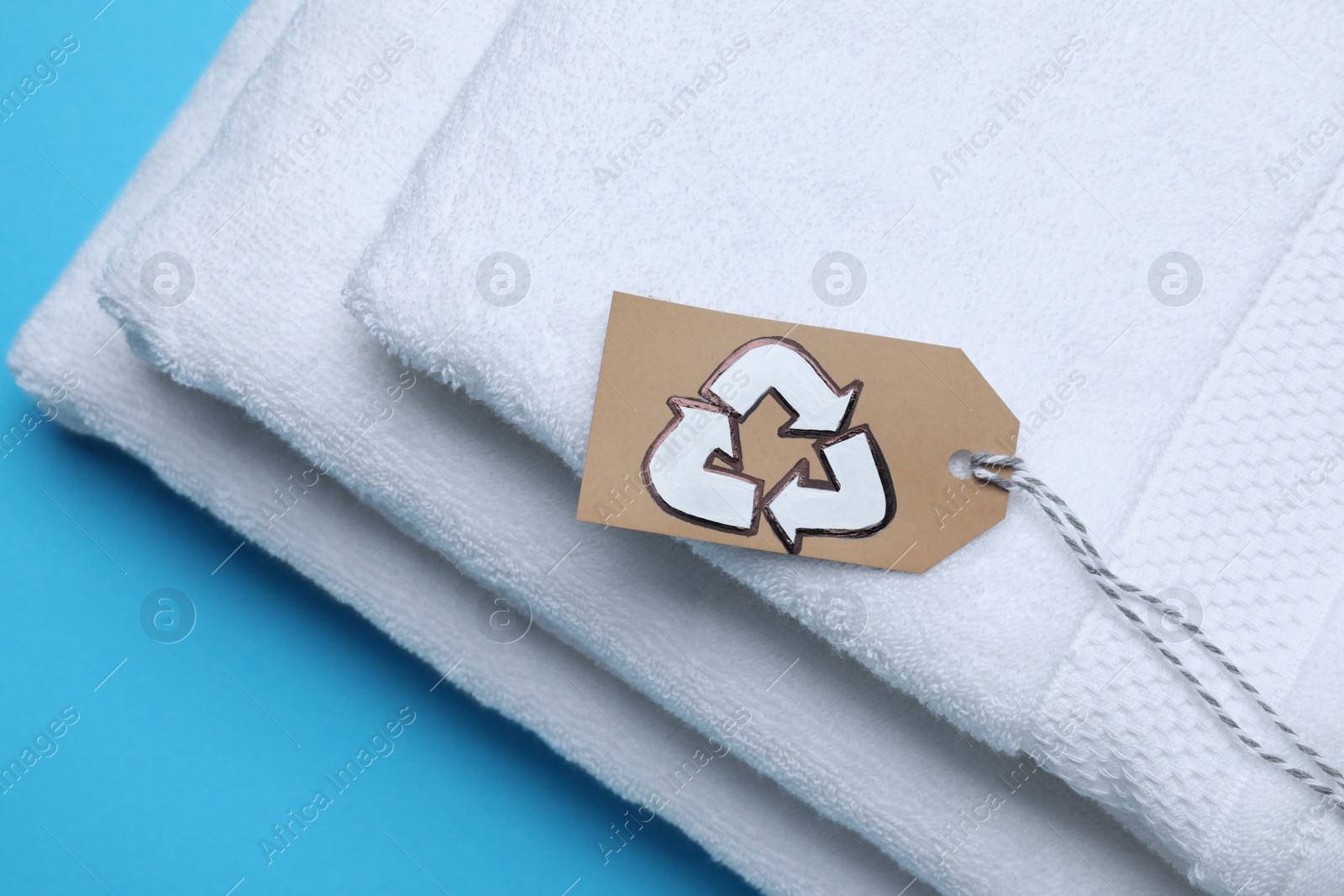 Photo of Stacked towels with recycling label on light blue background