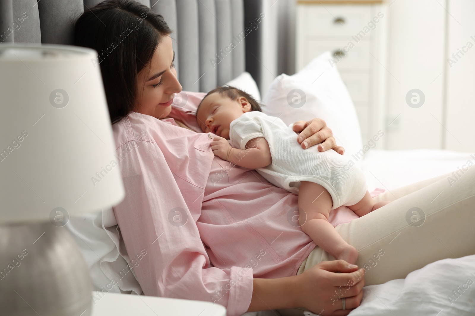 Photo of Mother with her sleeping newborn baby in bed at home