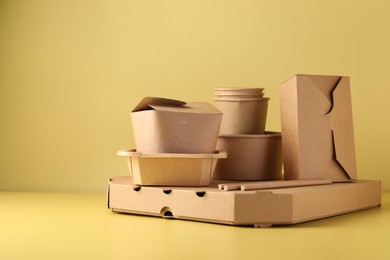 Photo of Eco friendly food packaging. Paper containers and tableware on pale yellow background, space for text