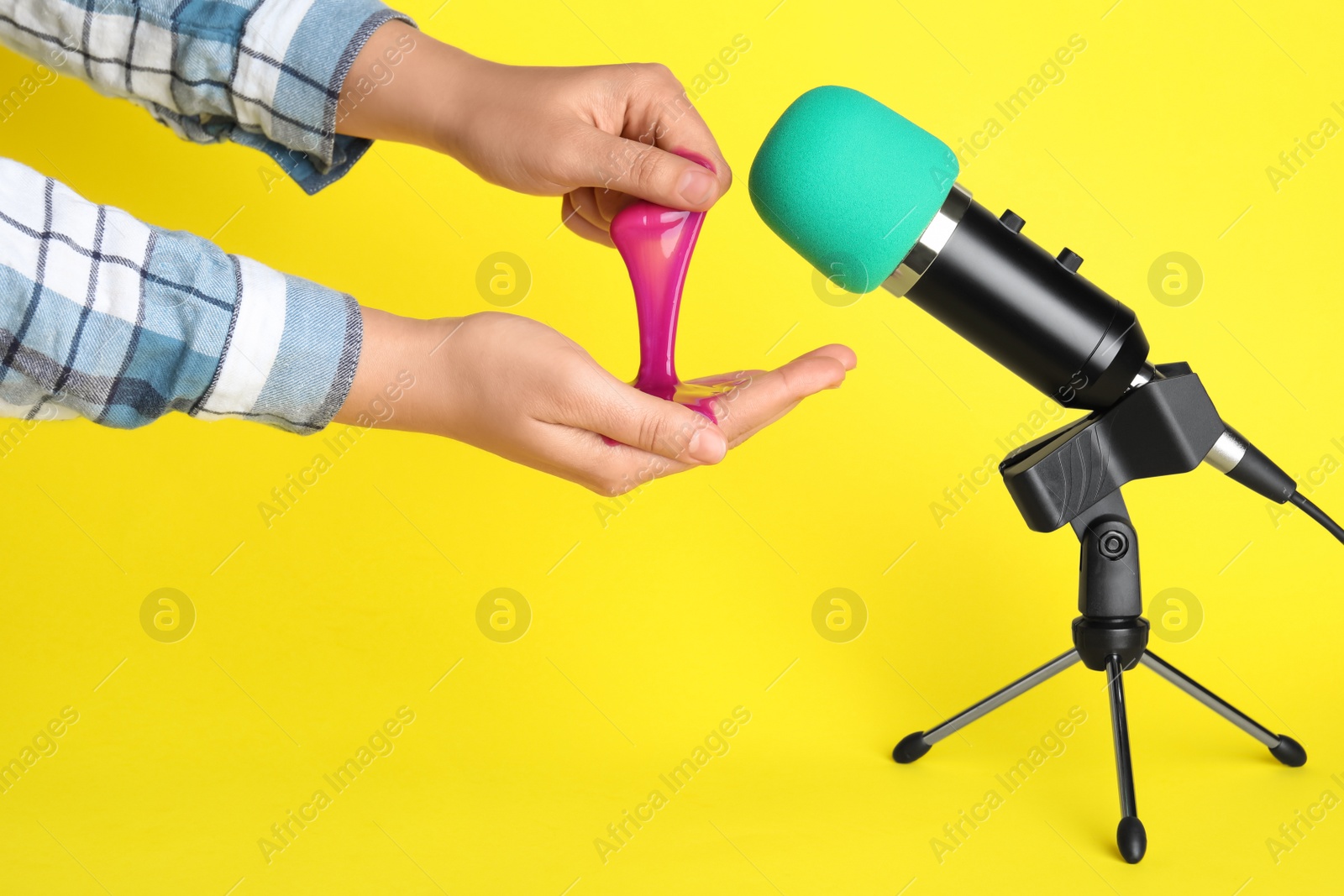 Photo of Woman making ASMR sounds with microphone and bright slime on yellow background, closeup