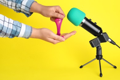 Photo of Woman making ASMR sounds with microphone and bright slime on yellow background, closeup
