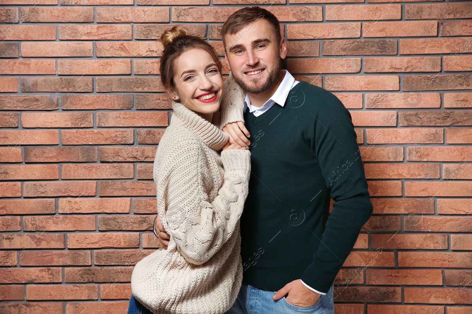 Photo of Young couple in warm sweaters near brick wall